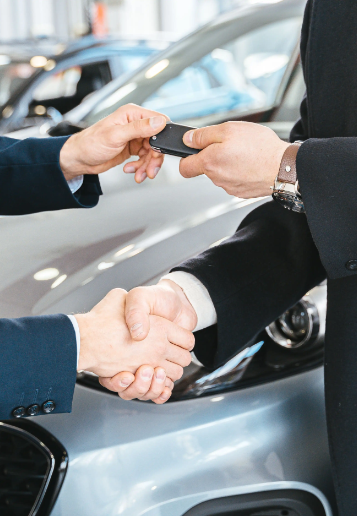 Car salesman handing over keys and shaking hands with a buyer at a dealership