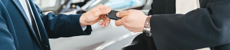 Car salesman handing over keys and shaking hands with a buyer at a dealership