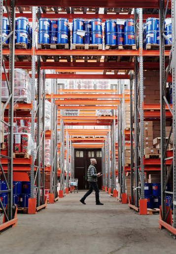 Staff member walking through a warehouse aisle stocked with retail goods